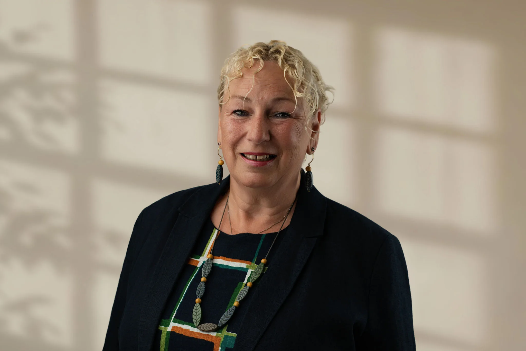 Woman with curly blond hair wearing a patterned top and dark jacket