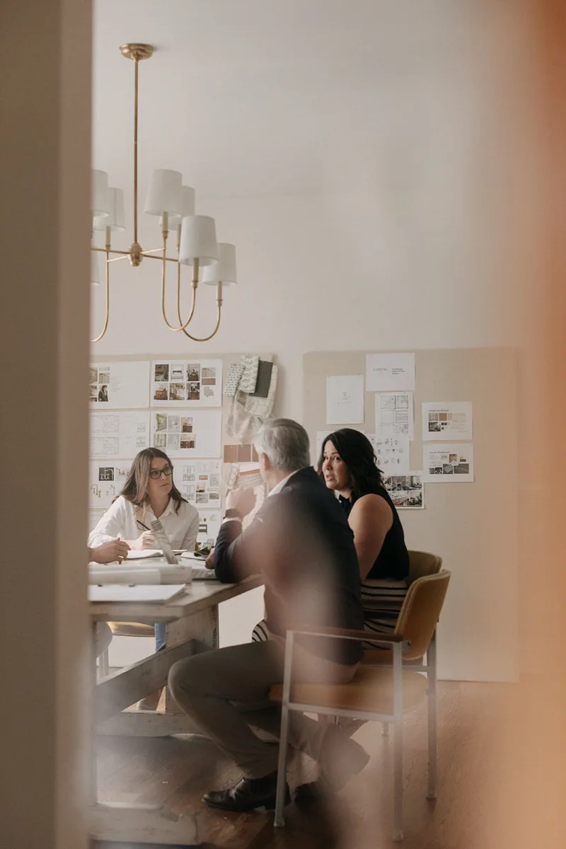 Three people in a meeting room with notes on the wall and chandelier overhead