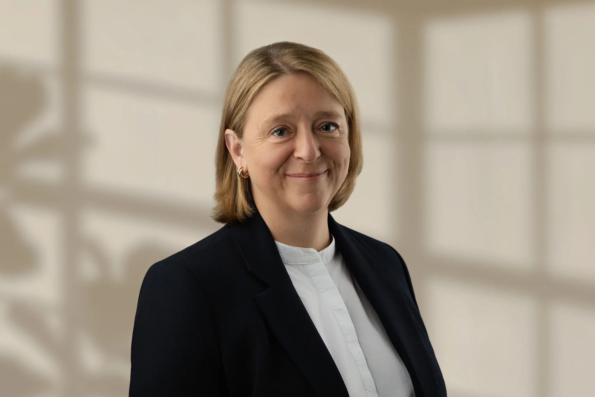 Jill Heywood wearing a dark blazer and white blouse against a beige background