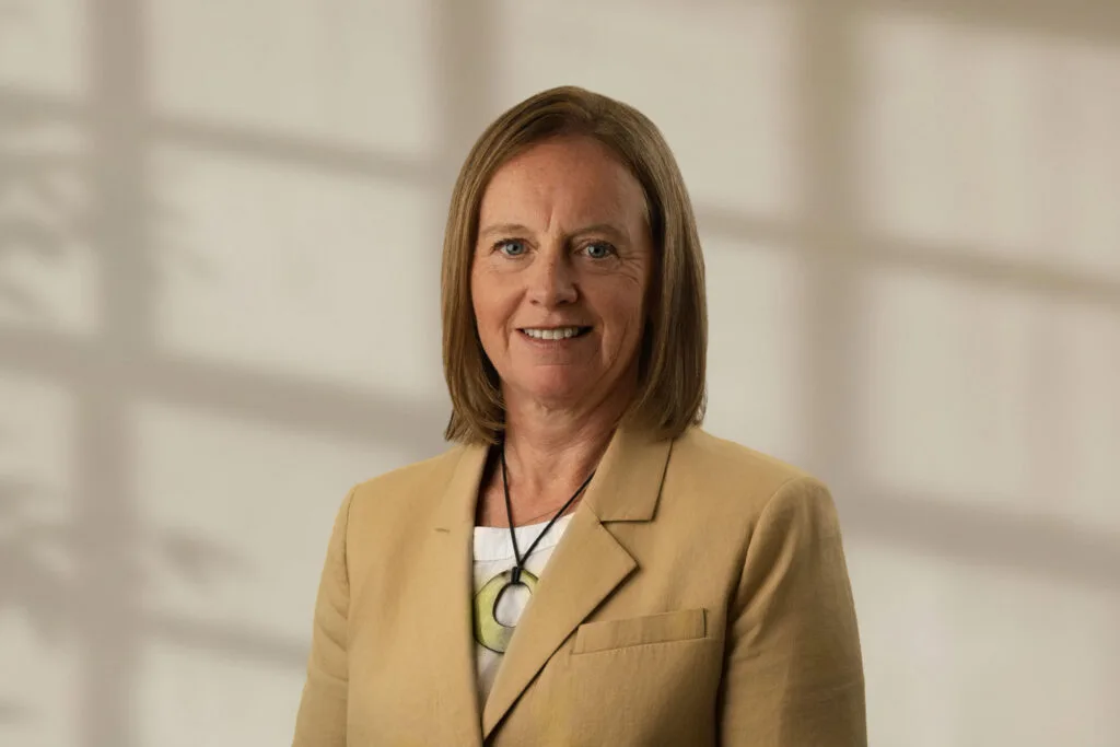 Nadia Kerr with shoulder-length light brown hair wearing a beige blazer and necklace