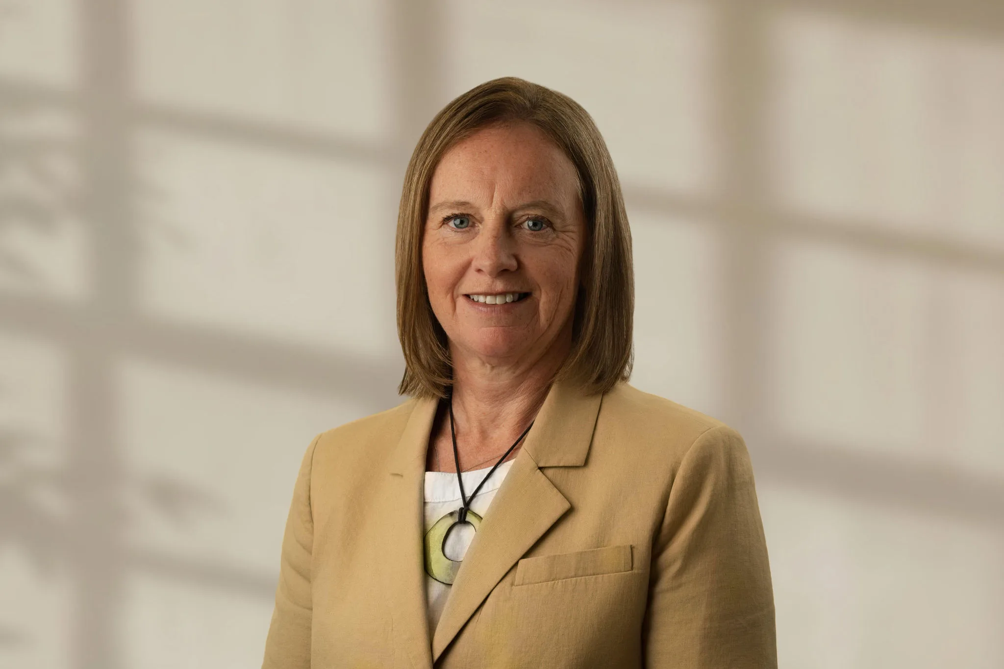 Nadia Kerr with shoulder-length light brown hair wearing a beige blazer and necklace