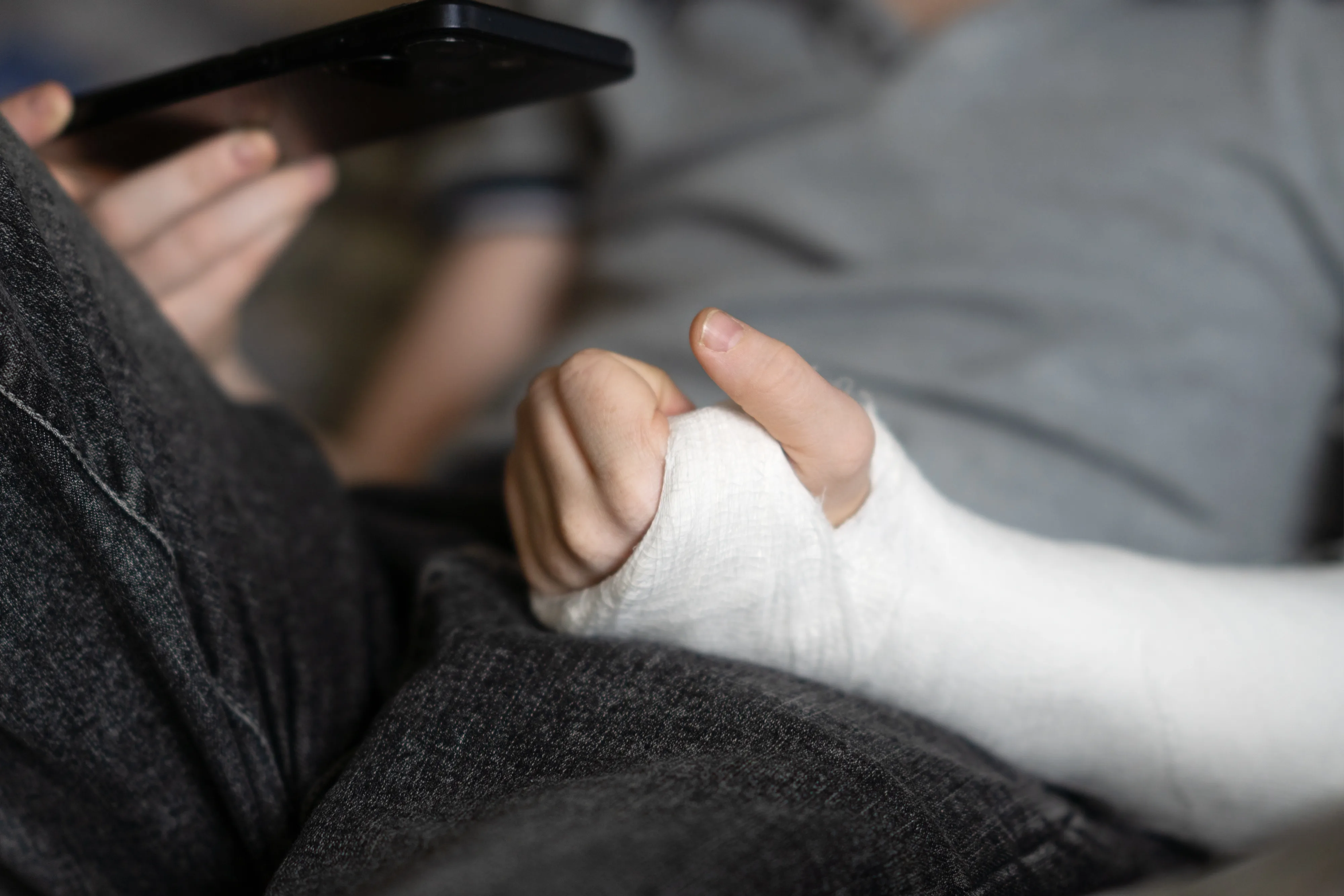 Close-up of hand in white plaster cast resting on person's lap