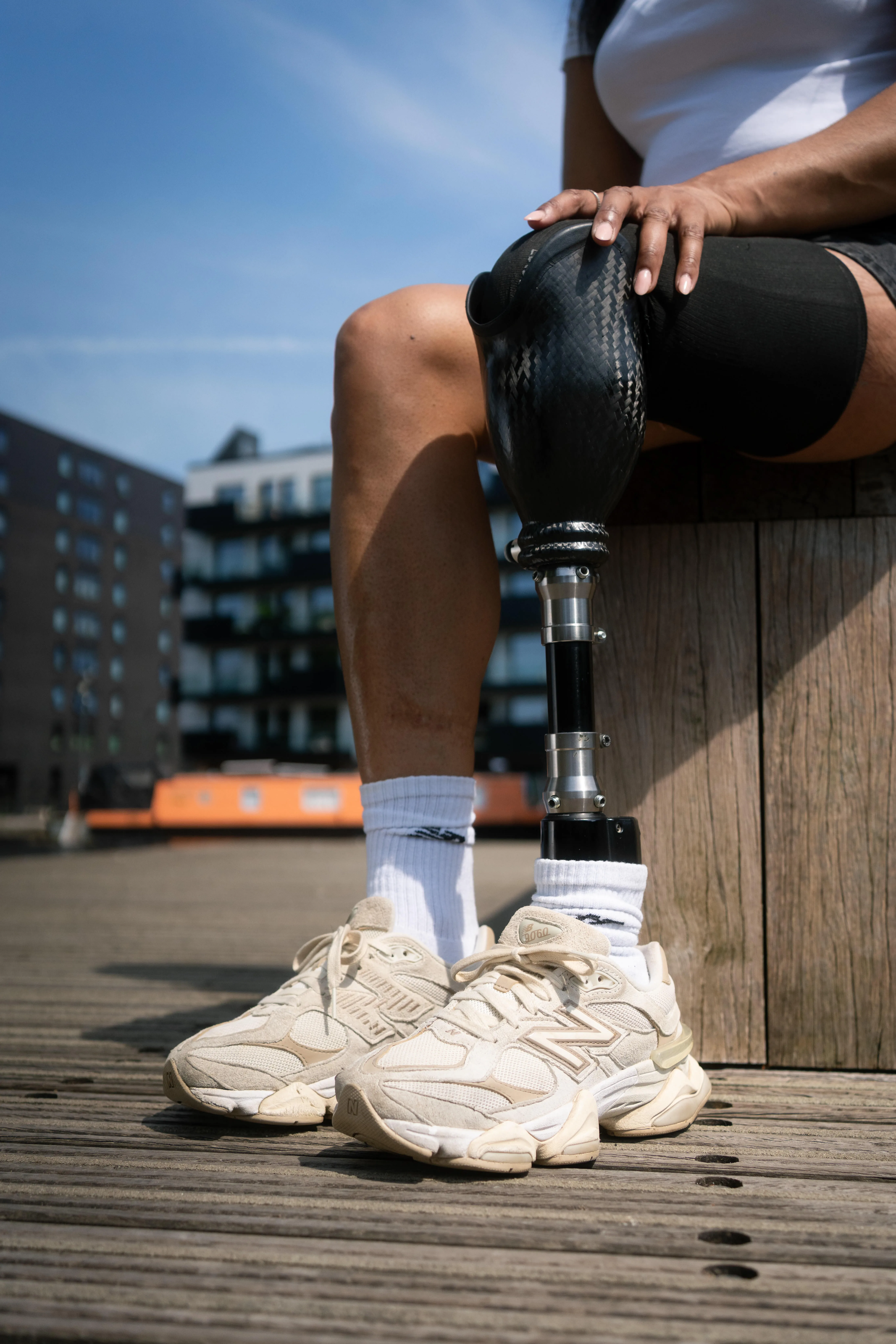 Person with prosthetic leg sitting outdoors wearing white trainers and black shorts