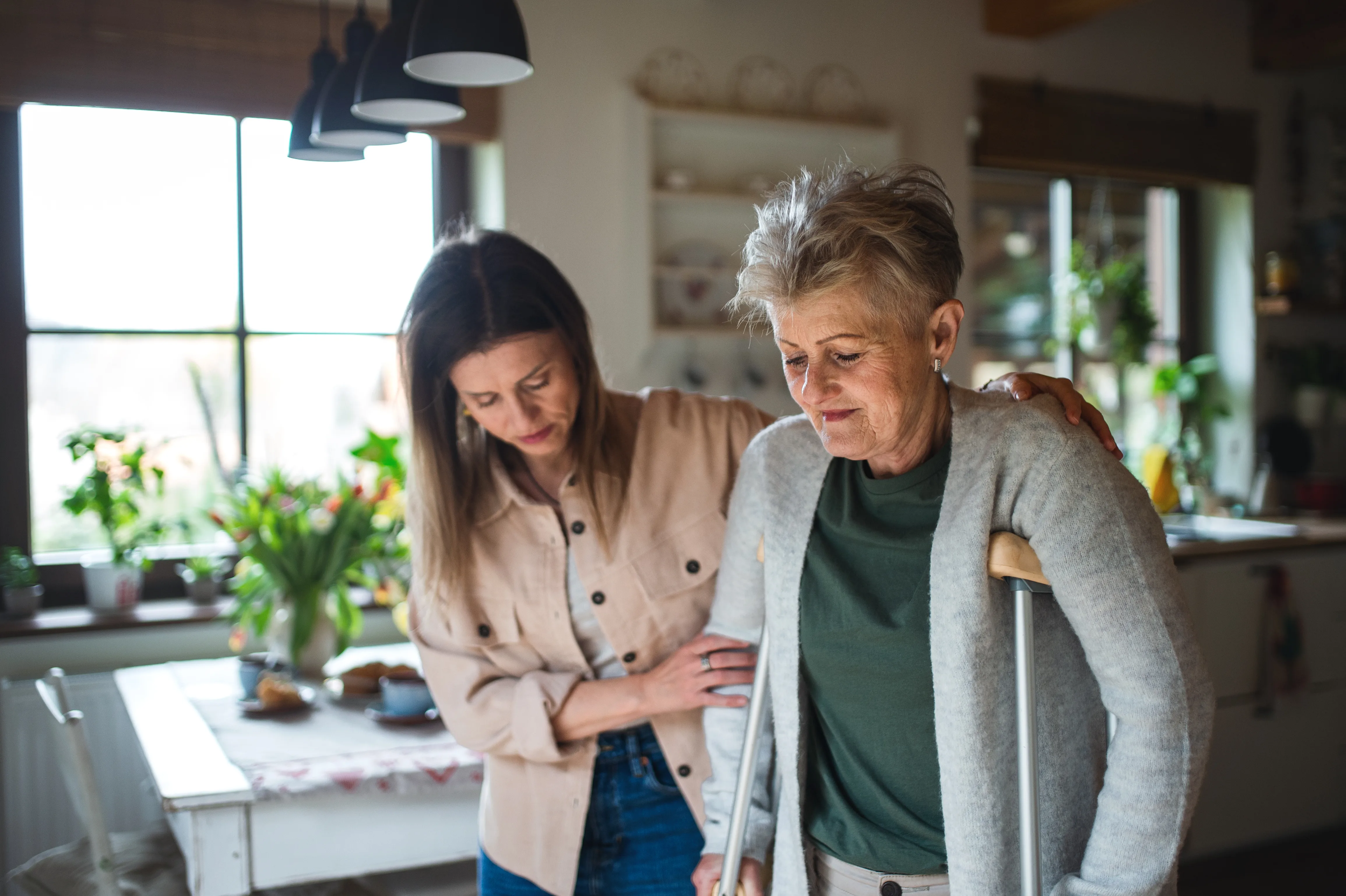 Woman supporting senior woman with crutches inside a home