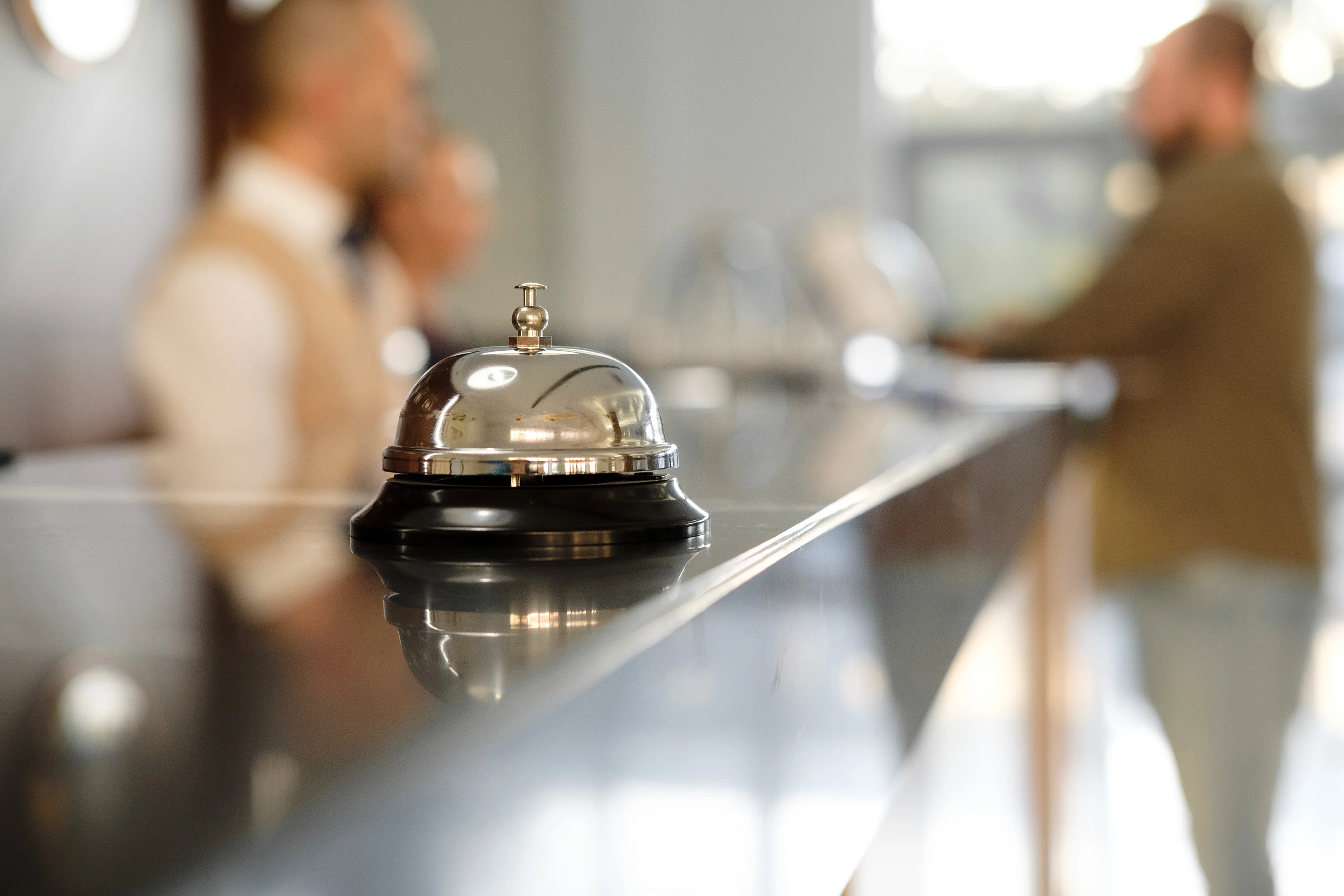 Reception bell on hotel counter with blurred staff and guest in background