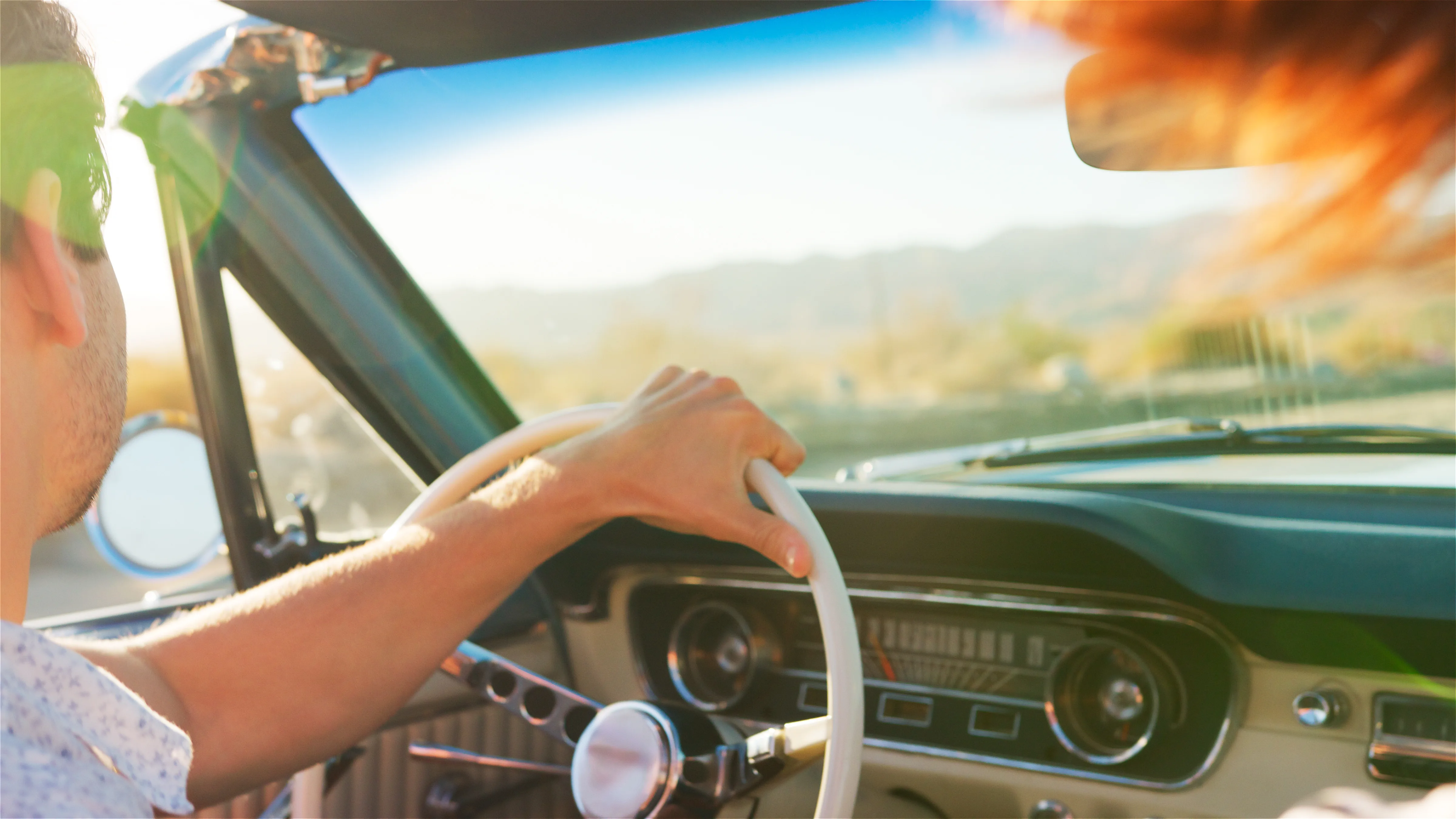 Person driving a cream vintage convertible car with sunlight glare