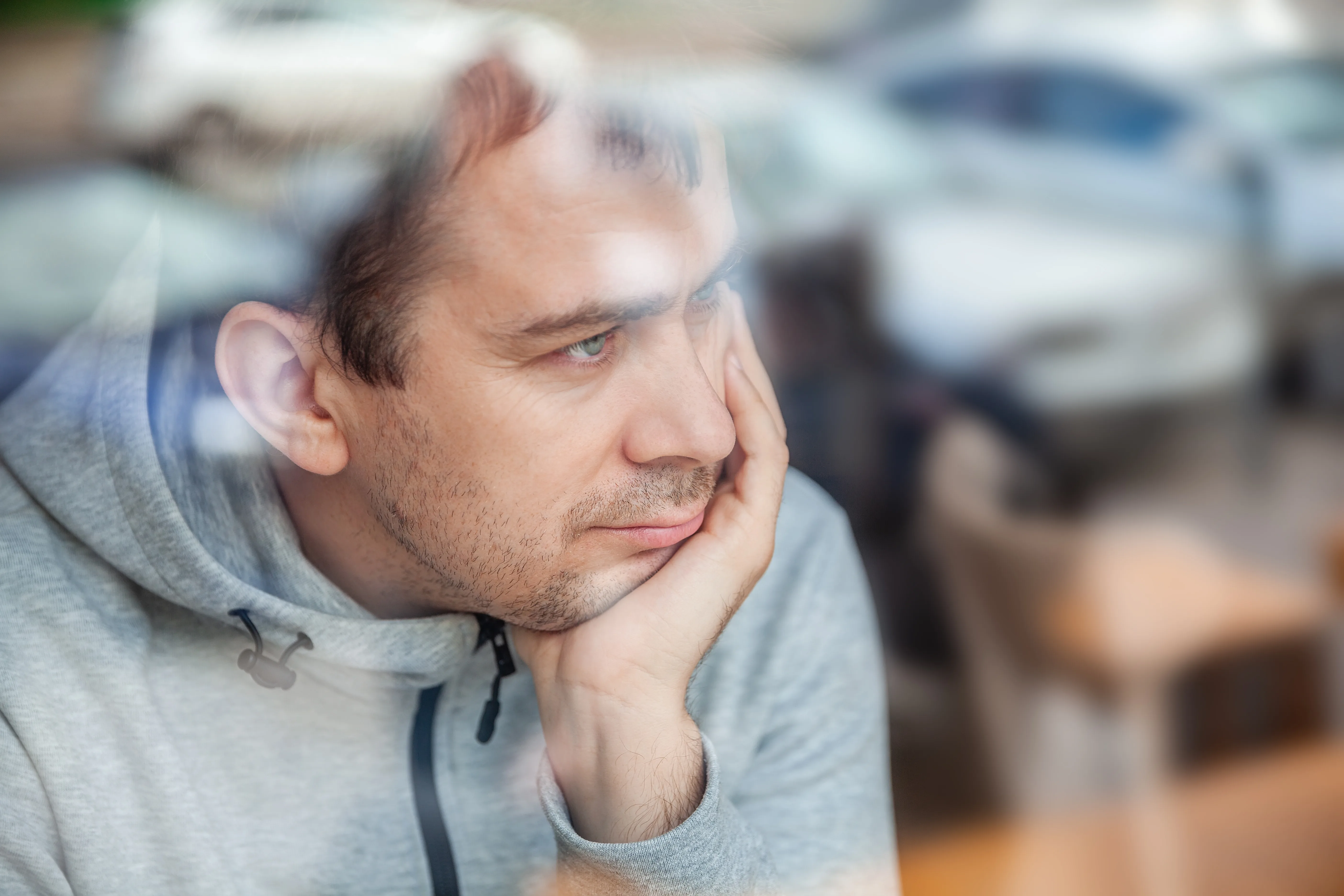 Man leaning head on hand, looking pensively through a window in a café
