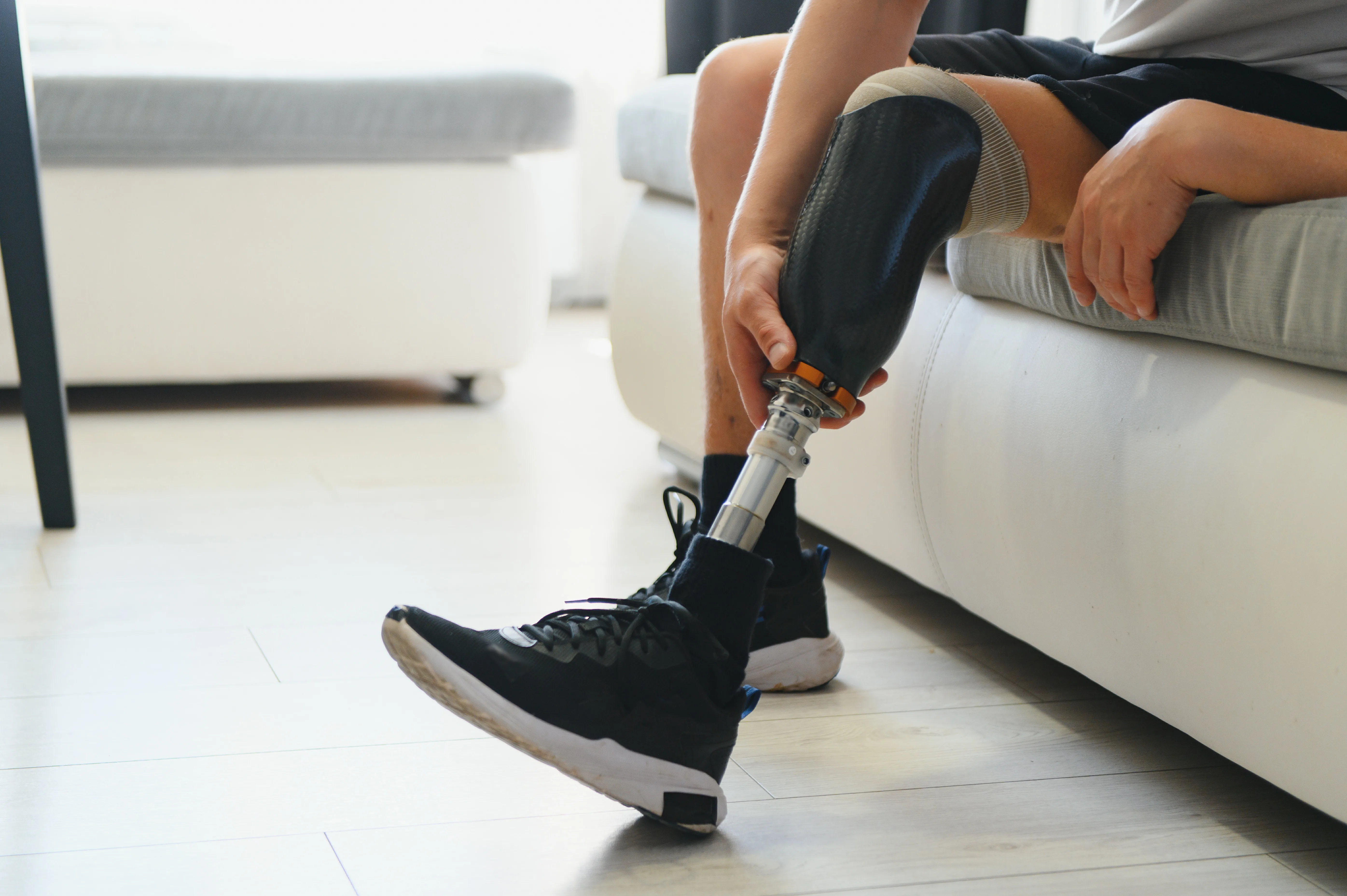 Person adjusting prosthetic leg while seated on sofa