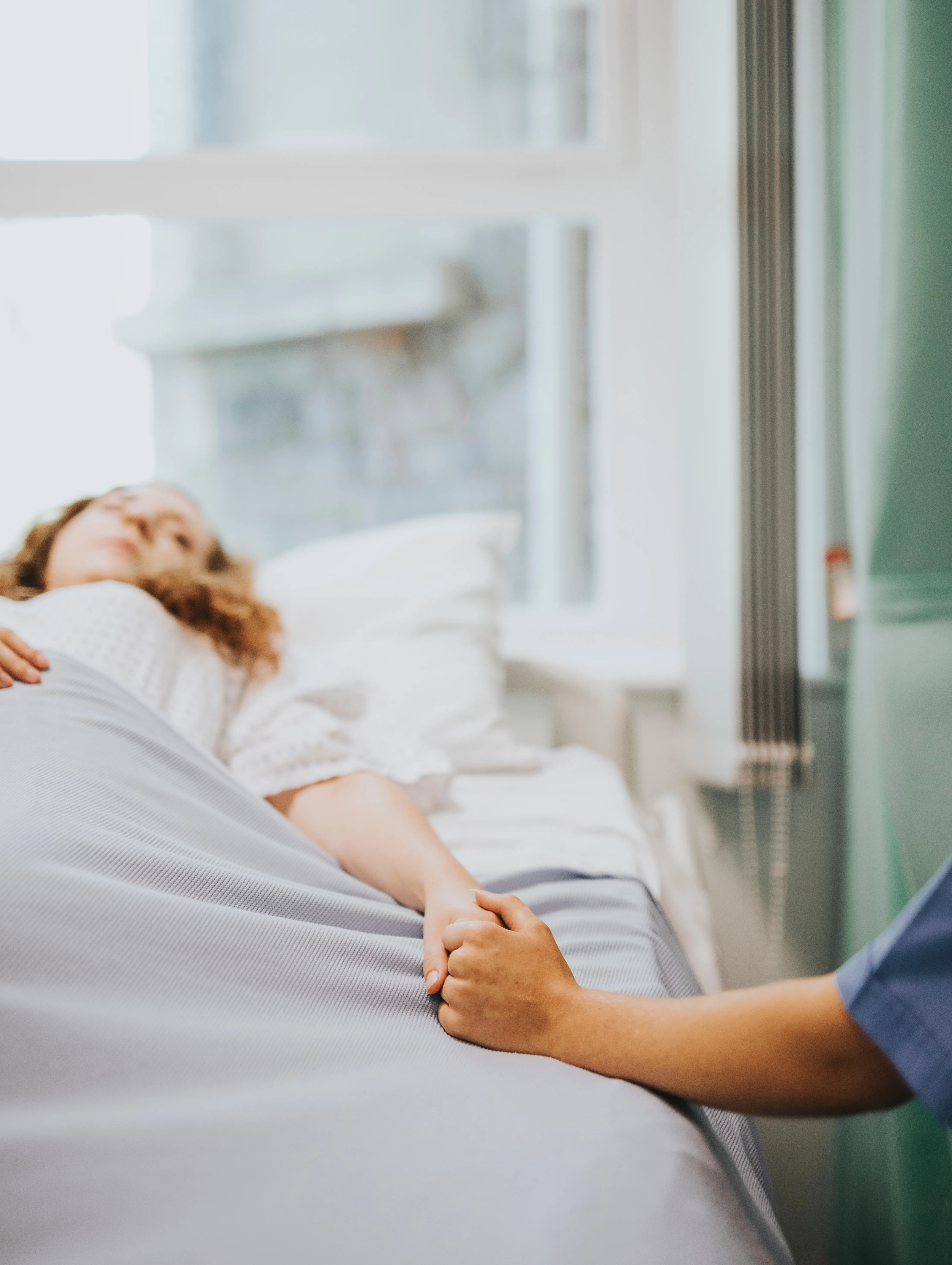 Nurse holding hand of patient lying in hospital bed