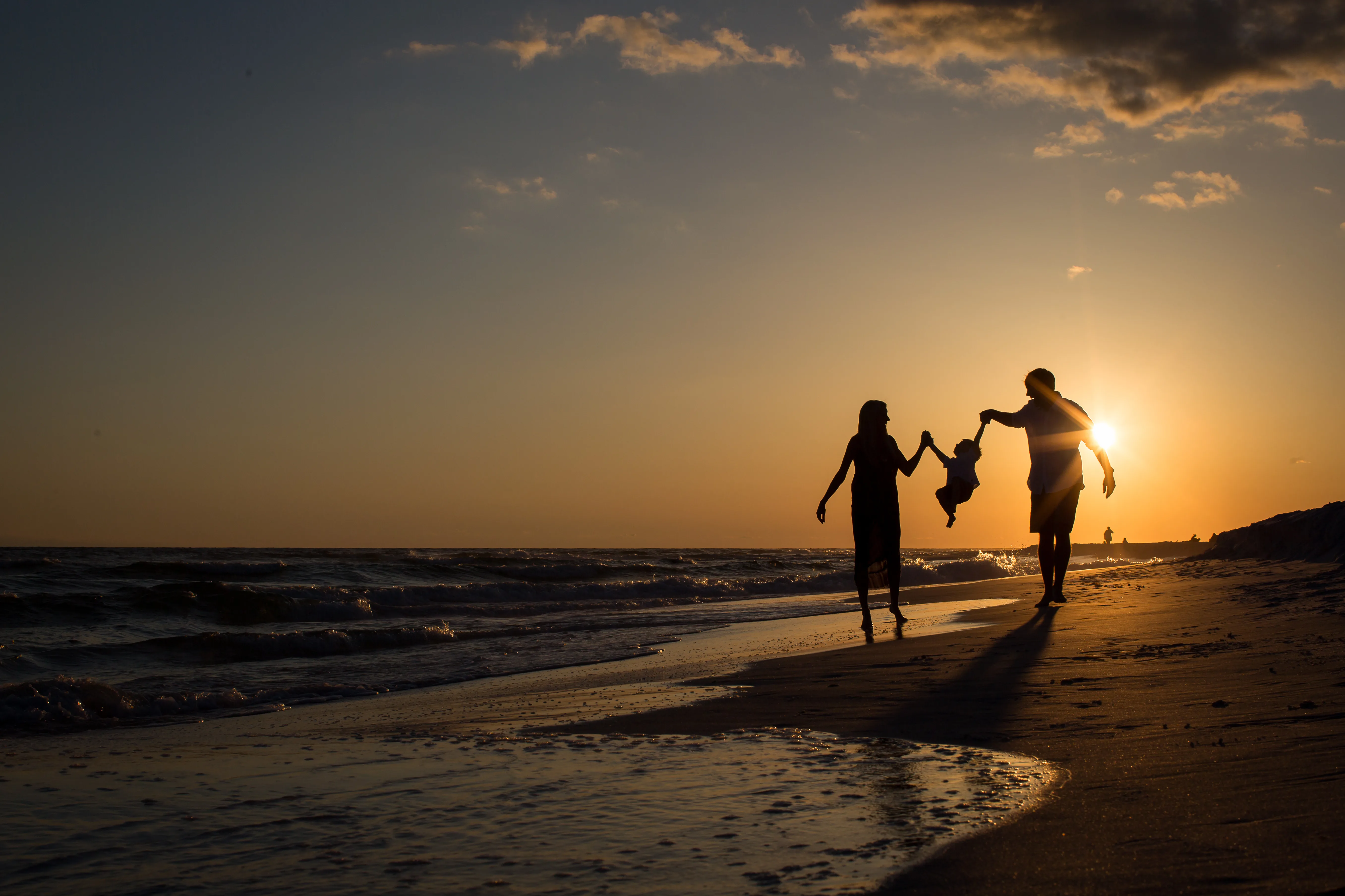 Silhouetted family walking on the beach at sunset holding hands with child swinging