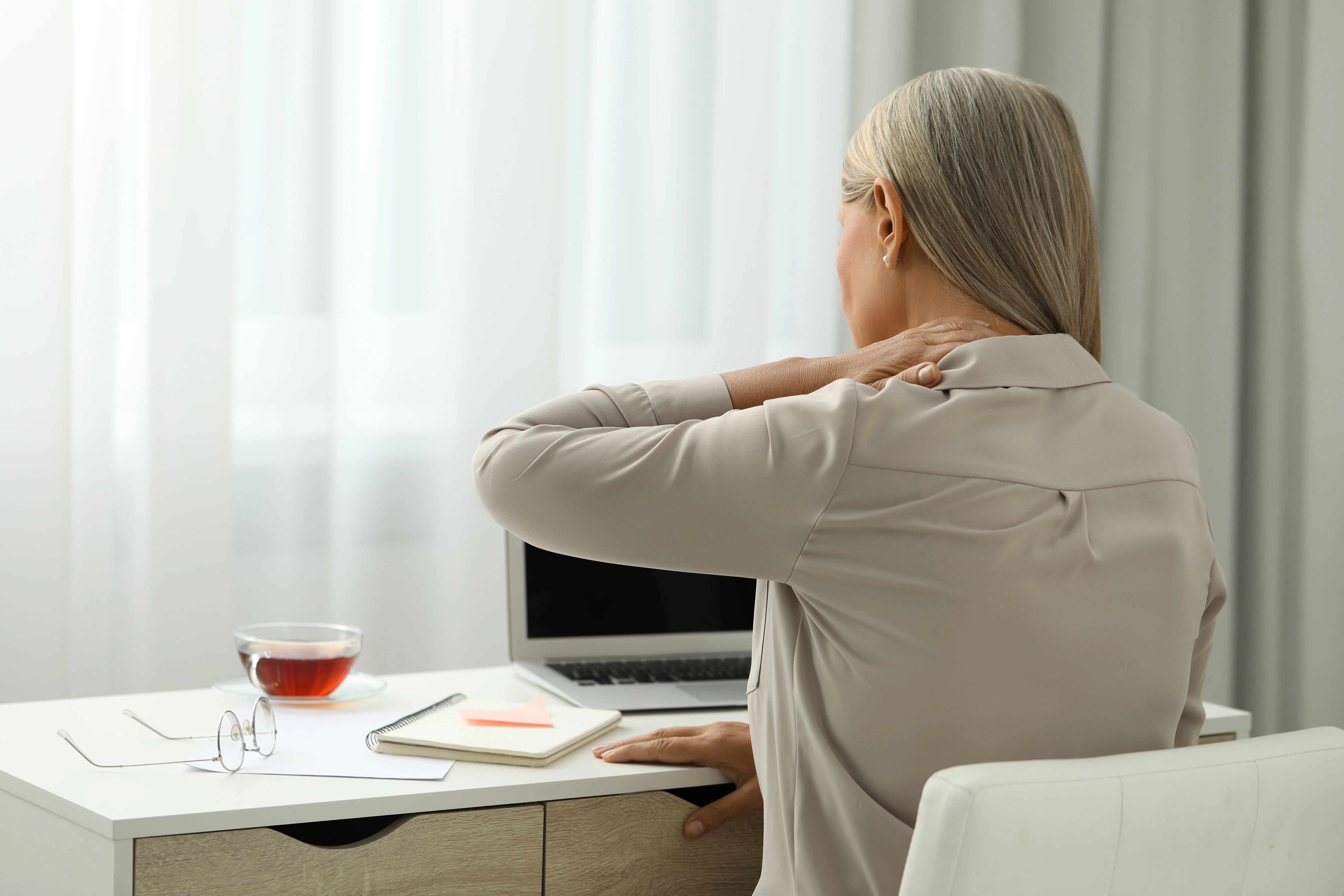 Woman in office sitting at desk holding neck in pain