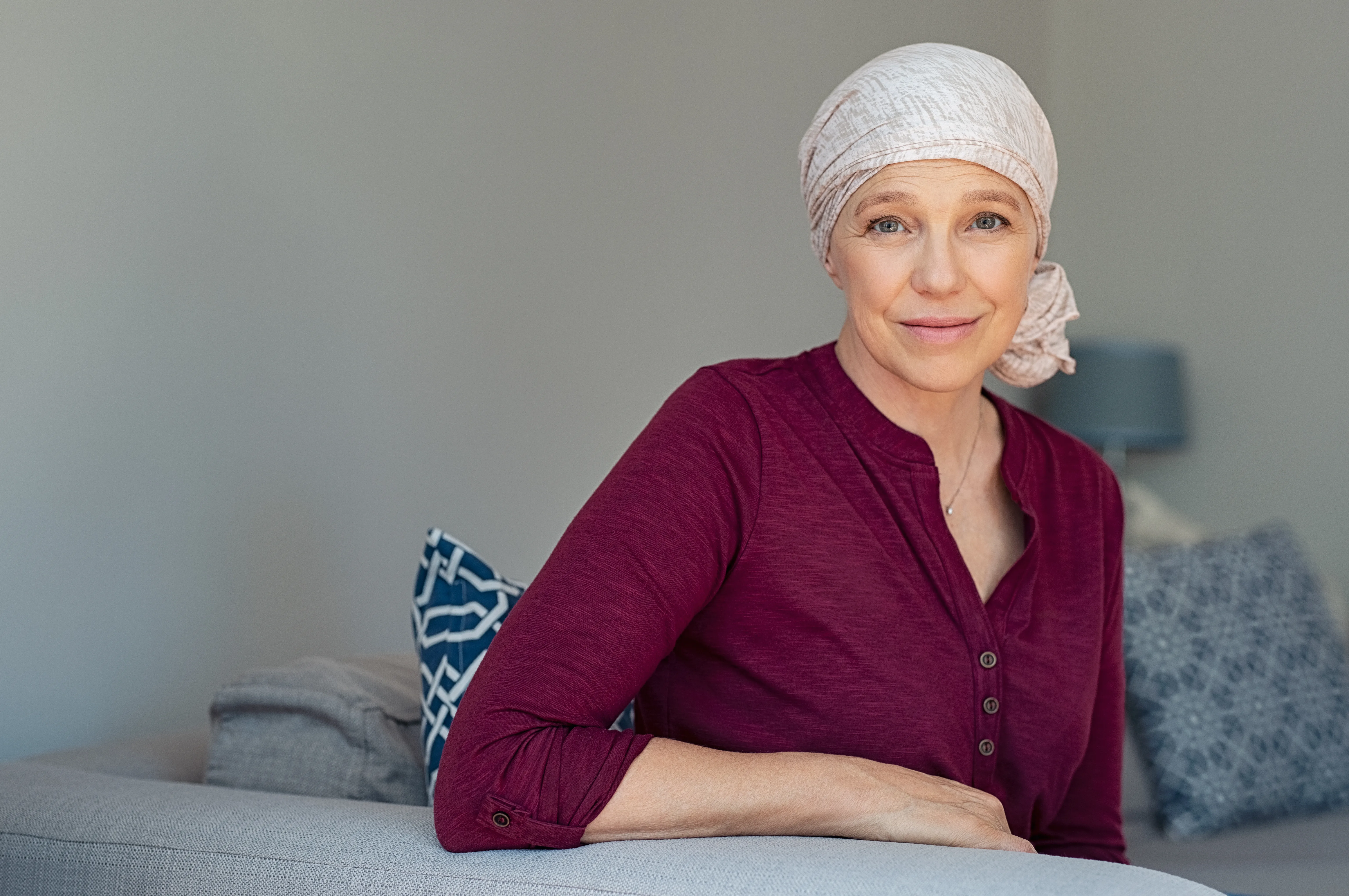 Woman with light headscarf and red top sitting on a sofa looking at camera