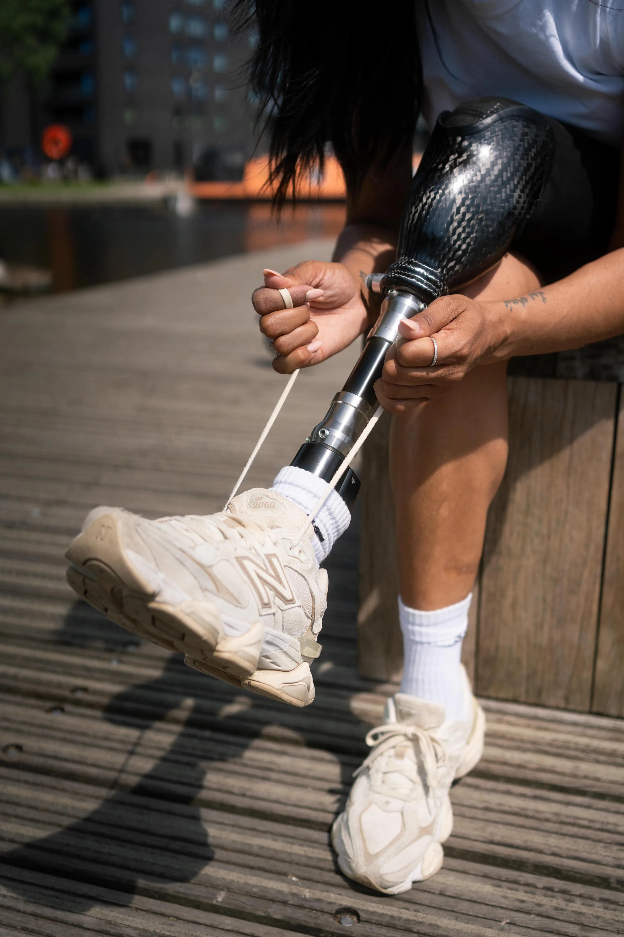Person tying shoelaces on left foot with carbon fibre prosthetic leg outdoors