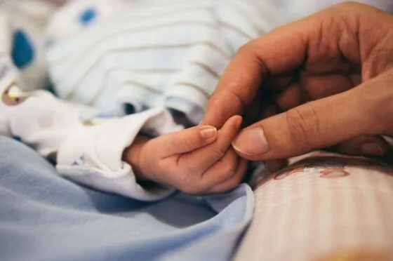 Adult holding baby's hand in hospital