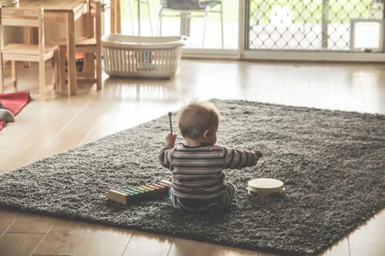 Child sitting on rug with toy piano