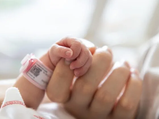 Newborn baby holding adult finger