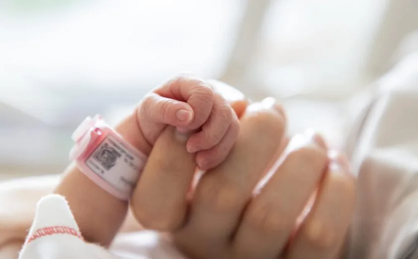 Newborn baby holding adult finger