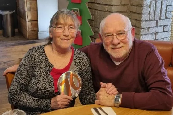 Older couple seated at table holding rainbow ornament