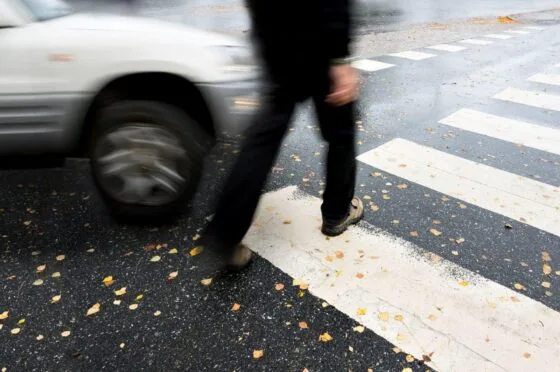 Pedestrian crossing road near passing car