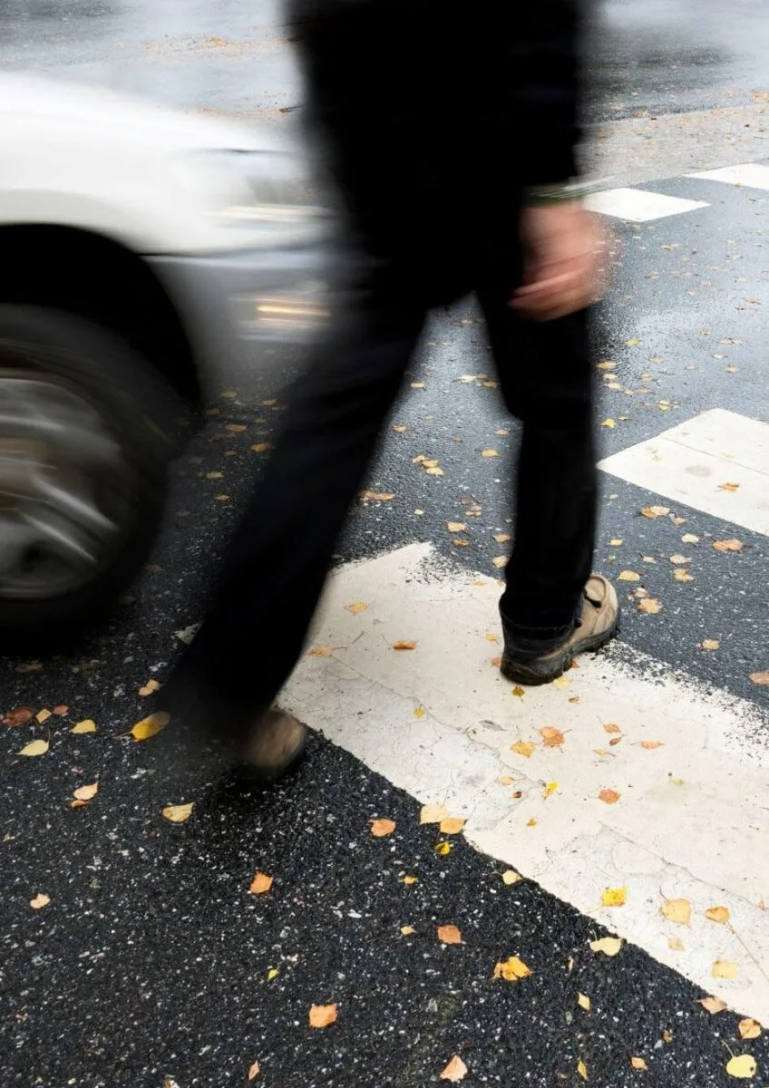 Pedestrian crossing road near passing car