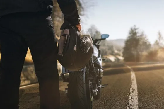 Rider holding helmet beside motorcycle