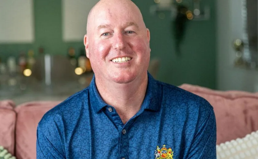 Smiling man seated at home wearing blue polo shirt
