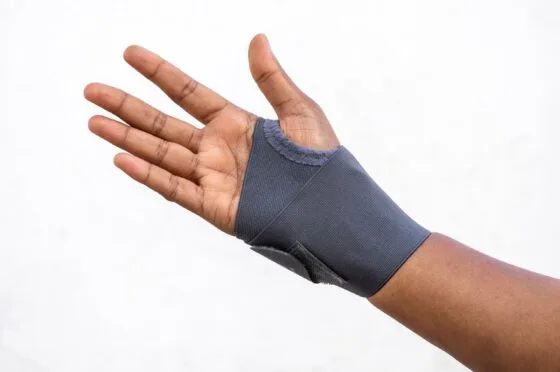 Hand wearing a grey wrist support brace against white background