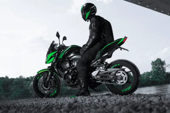 Motorcyclist in black gear and helmet sitting on a black and green motorcycle near a river under a structure
