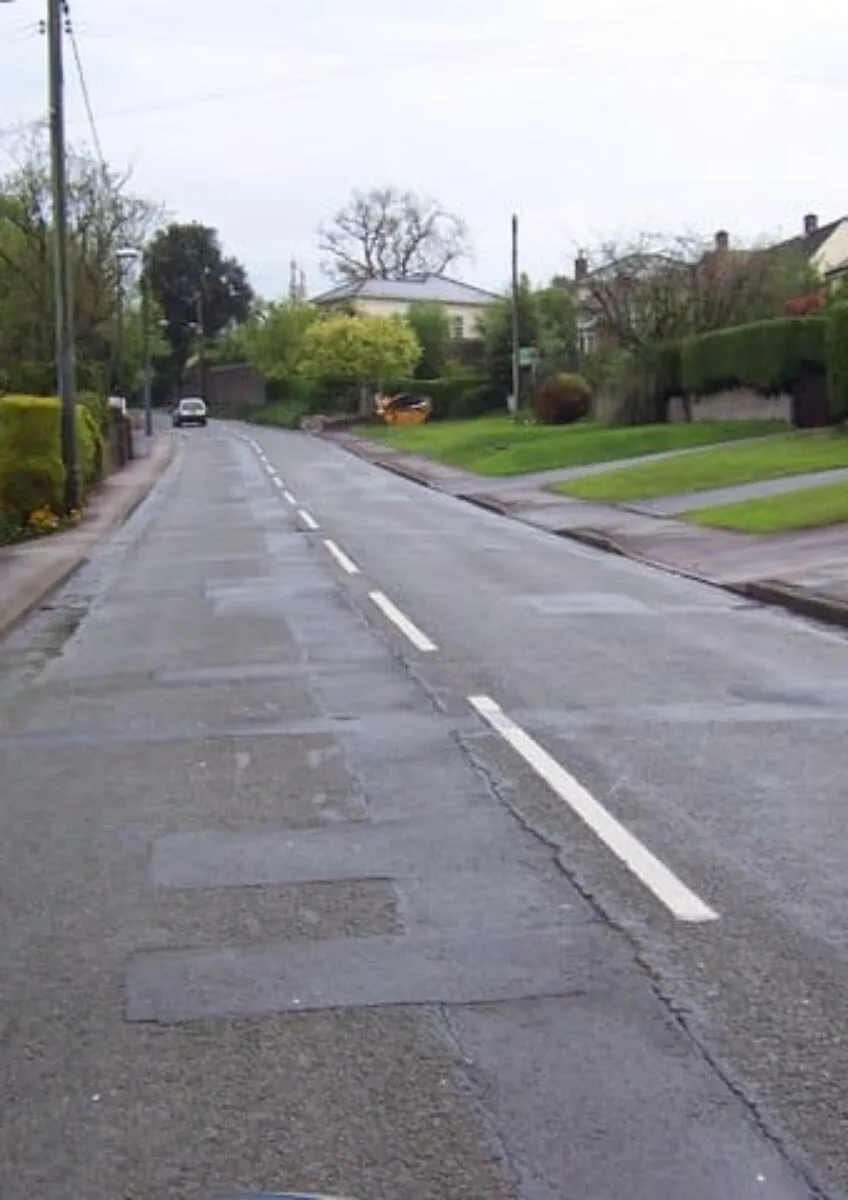 Empty residential street lined with houses and grassy gardens under cloudy sky