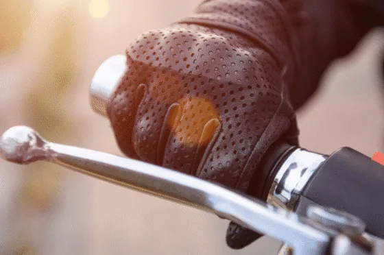 Gloved hand gripping motorcycle handlebar and brake lever in sunlight