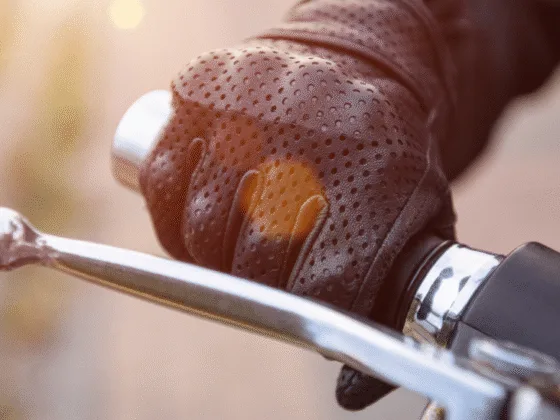 Gloved hand gripping motorcycle handlebar and brake lever in sunlight