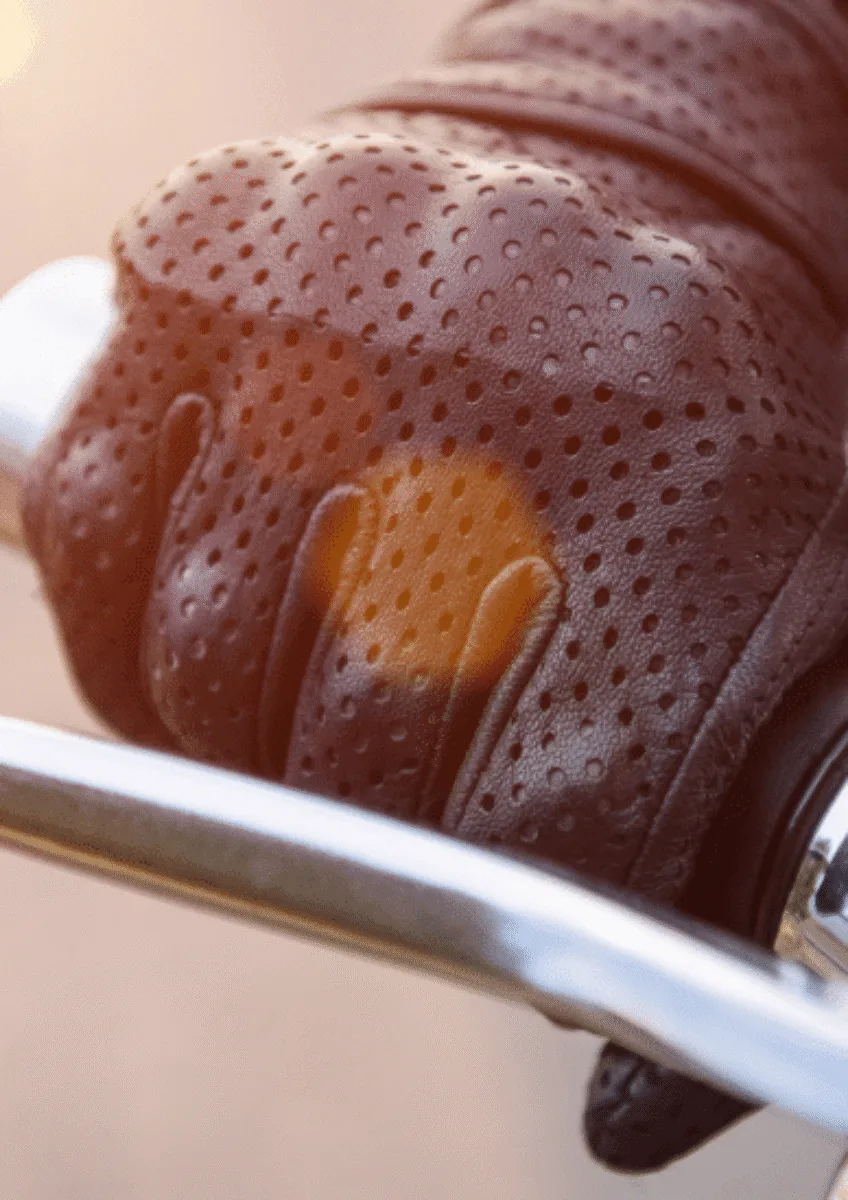 Gloved hand gripping motorcycle handlebar and brake lever in sunlight