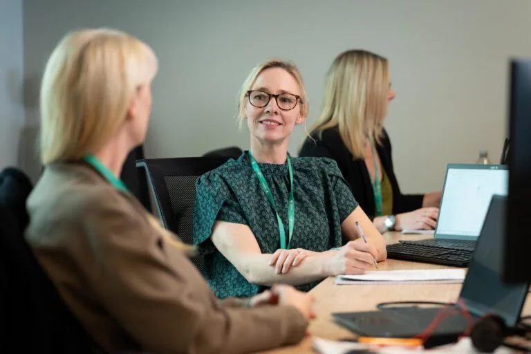 Two female colleagues have a conversation at their desks
