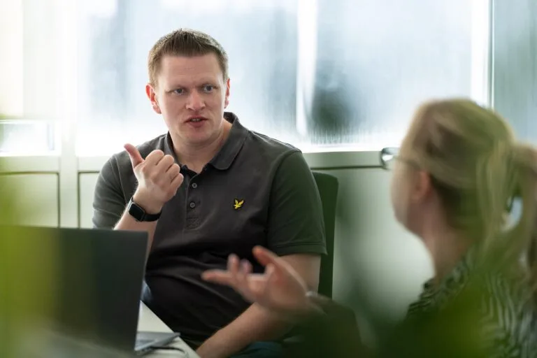 A male and female having a conversation at their desks