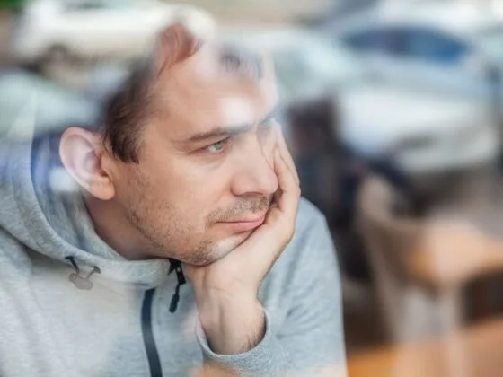 Man leaning head on hand, looking pensively through a window in a café