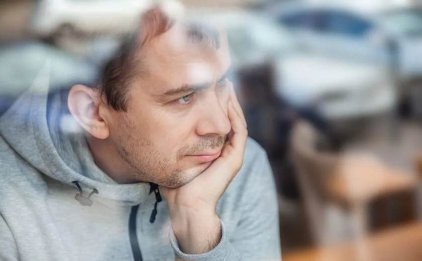 Man leaning head on hand, looking pensively through a window in a café
