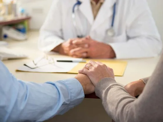 Two people holding hands in consultation with doctor at desk