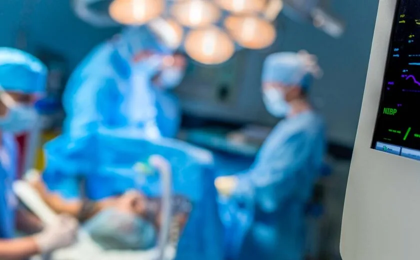 Blurred surgical team operating in brightly lit operating theatre with medical monitor in foreground
