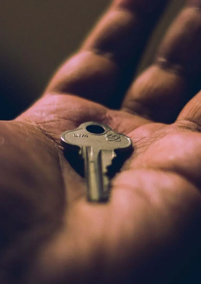 Close-up of hand holding small silver key on palm with dark background