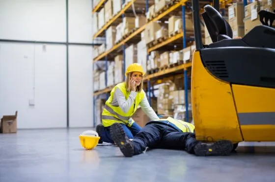 Female worker calling for help beside a male worker lying injured in warehouse