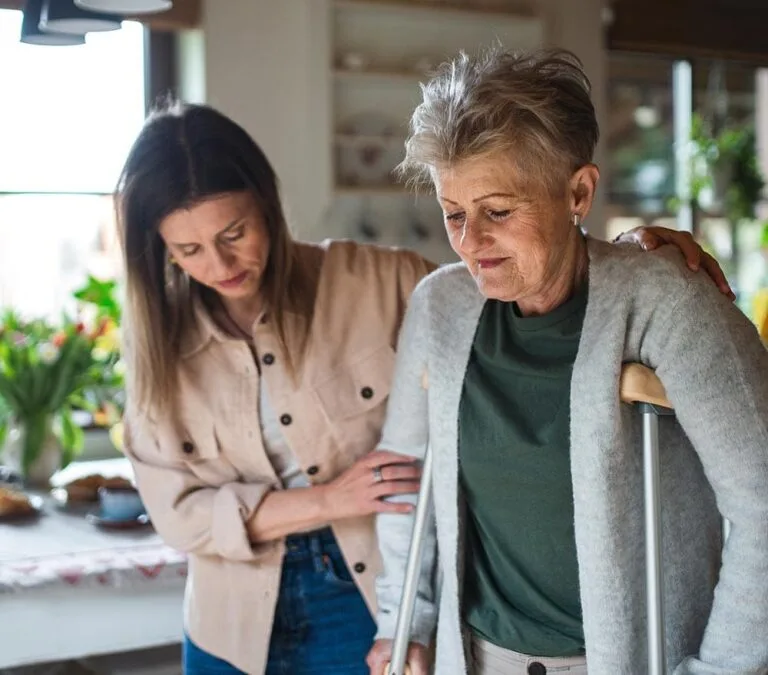 Woman supporting senior woman with crutches inside a home