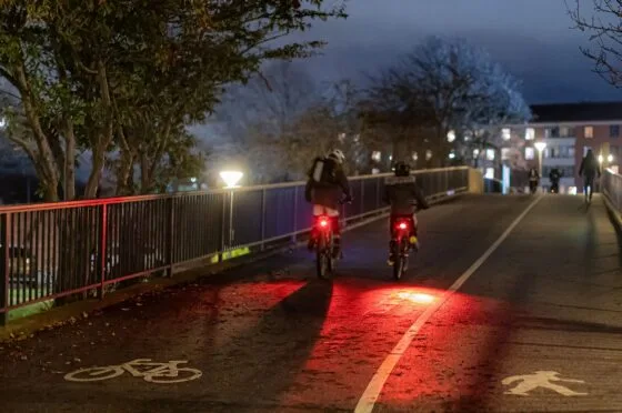 Cyclists riding in dark cycle lane over a bridge.