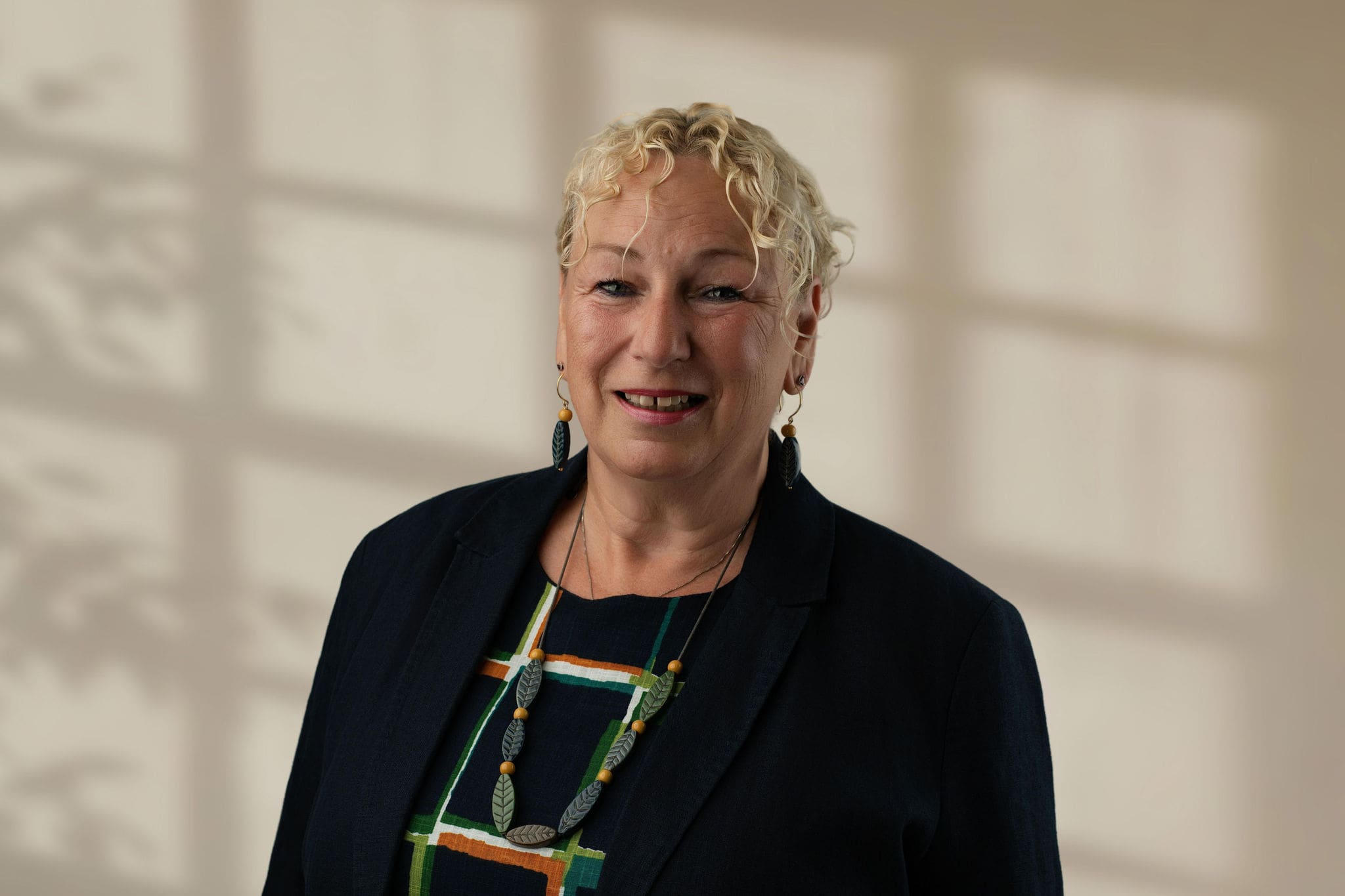 Woman with curly blond hair wearing a patterned top and dark jacket