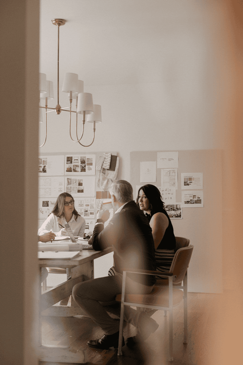 Three people in a meeting room with notes on the wall and chandelier overhead