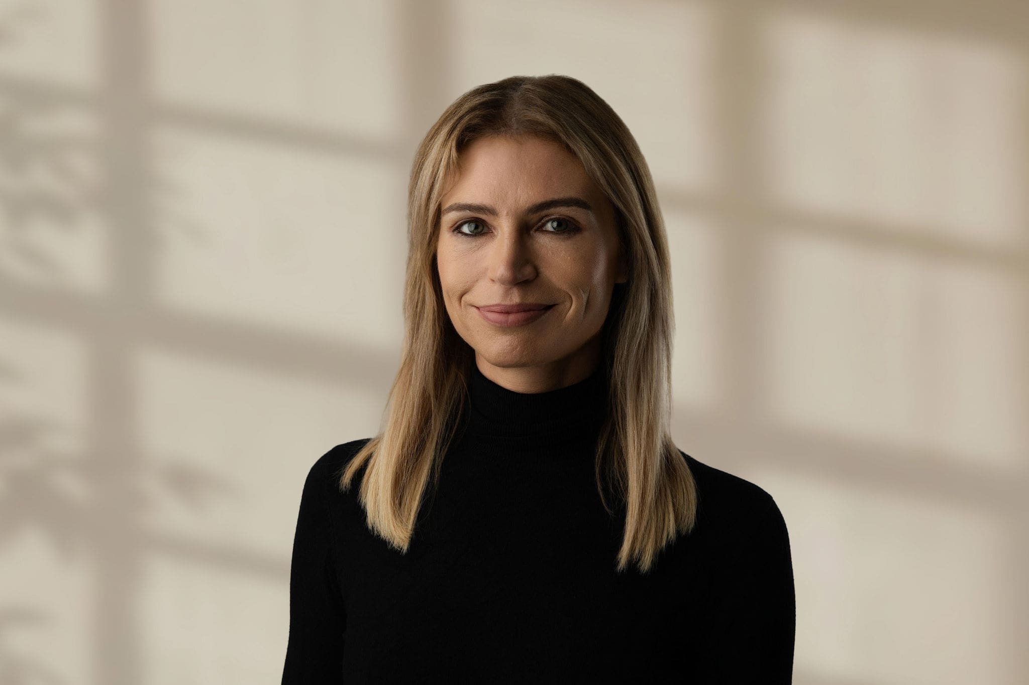 Alex Lynch wearing a black turtleneck sweater against a beige background