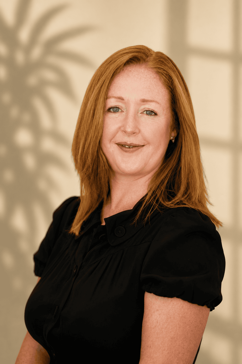Red-haired woman wearing a black blouse poses against a softly lit neutral background