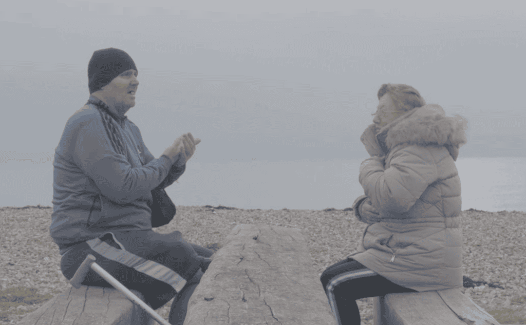Man and woman sitting opposite each other on wooden benches by the sea
