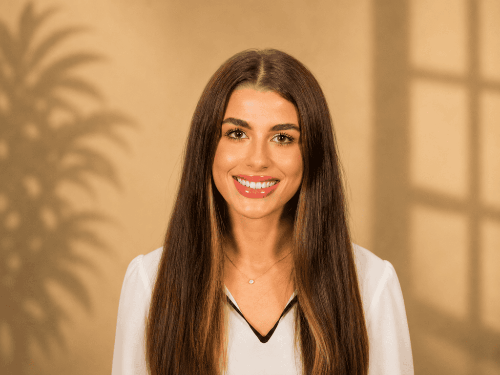 Young woman with long brown hair smiling against beige background