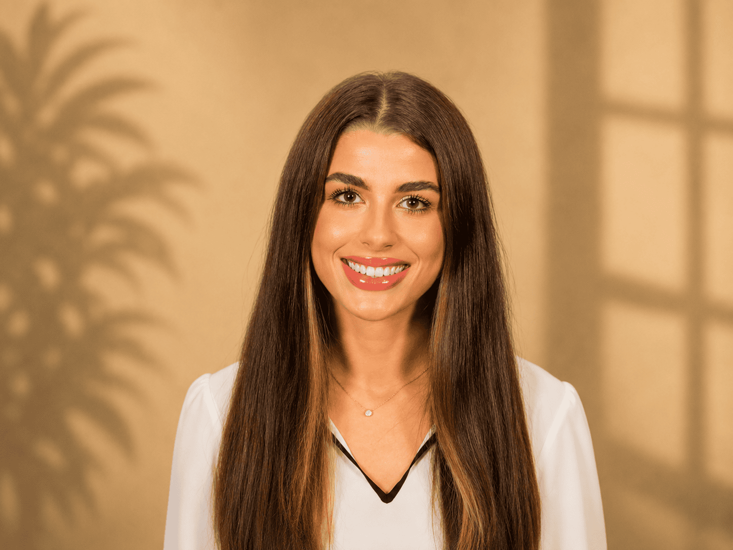Young woman with long brown hair smiling against beige background
