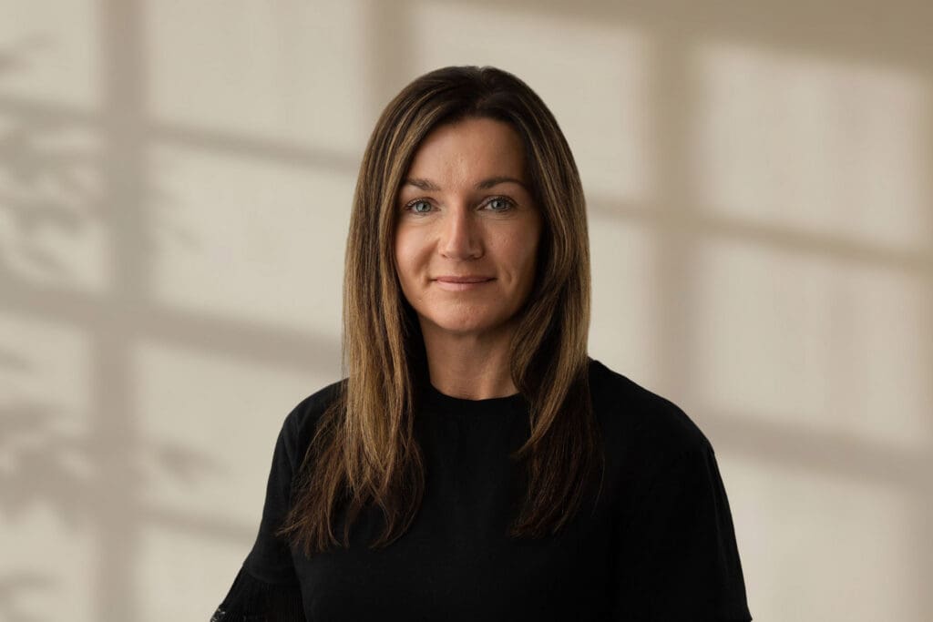 Lena Farnell looking at camera wearing a black top with straight light brown hair and a neutral expression